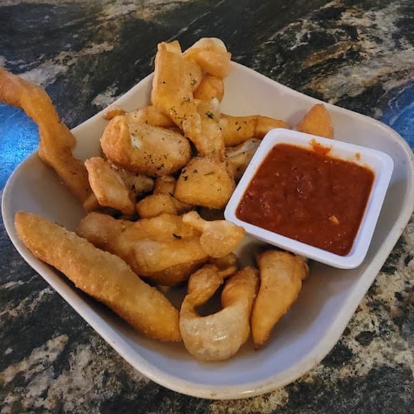 A white bowl of golden-brown fried dough pieces with a side of red marinara sauce.