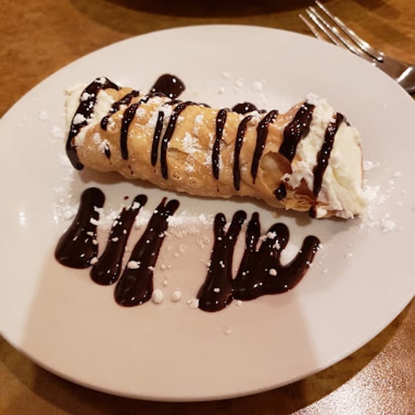 Ezio's Italian Restaurant cannoli, drizzled with chocolate sauce and powdered sugar on a white plate.