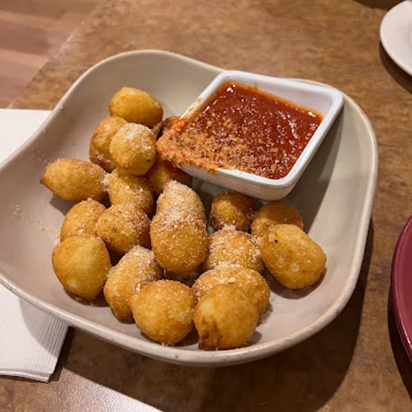 A bowl of golden-brown Italian cheese curds, dusted with Parmesan, served with a side of marinara sauce.