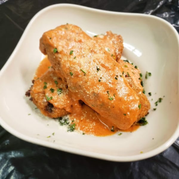 Two fried Italian appetizers covered in creamy orange sauce, parmesan, and parsley in a white dish.